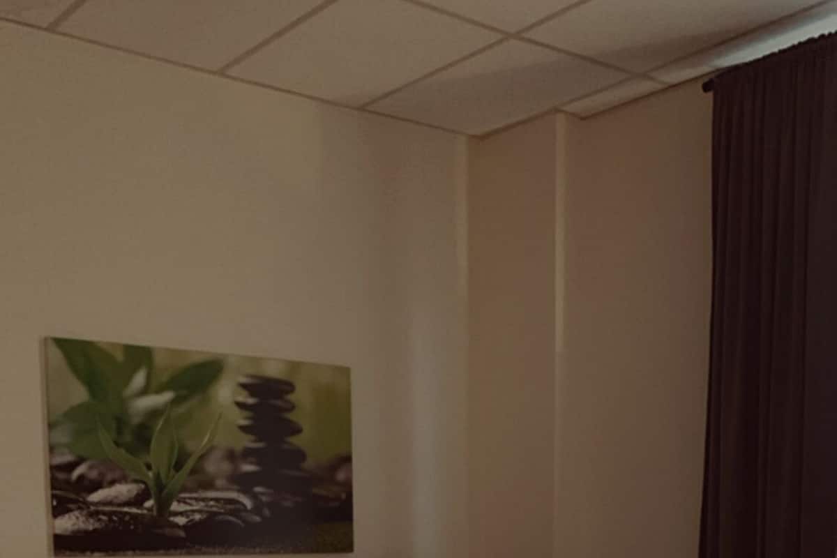 Habitación de hotel con cama, cabecera, un cuadro en la pared y una ventana con cortinas.