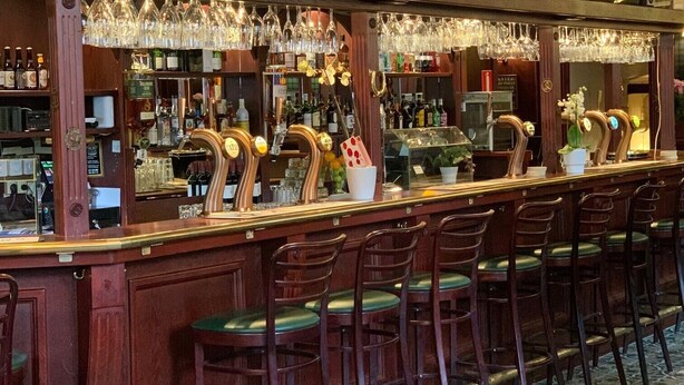 Un bar avec des comptoirs en bois, de nombreuses étagères remplies de bouteilles et un sol à motifs.