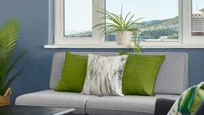 A modern living room with a grey sofa, a black coffee table, and a window with a view of a distant landscape. - Vibrant Tamboerskloof Gem with Table Mountain View (Cape Town)