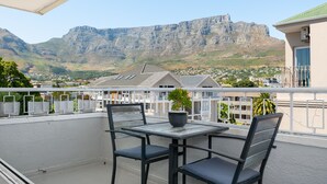 A balcony with a table and chairs, overlooking a town and mountains. - Vibrant Tamboerskloof Gem with Table Mountain View (Cape Town)