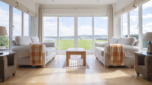 Een ruime woonkamer met twee banken, een salontafel en grote ramen met uitzicht op een groen landschap.