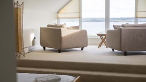 Een moderne hotelkamer met een groot raam met uitzicht op zee, een bank, een kleine tafel en een bed met netjes gevouwen handdoeken.