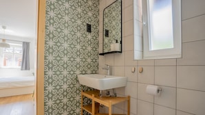 A bathroom with a patterned green and white wall, a white sink, a mirror, and a window. - HIŠANAVOGALU (AP.3)Cozy studio in Lesce, near Bled (Radovljica)