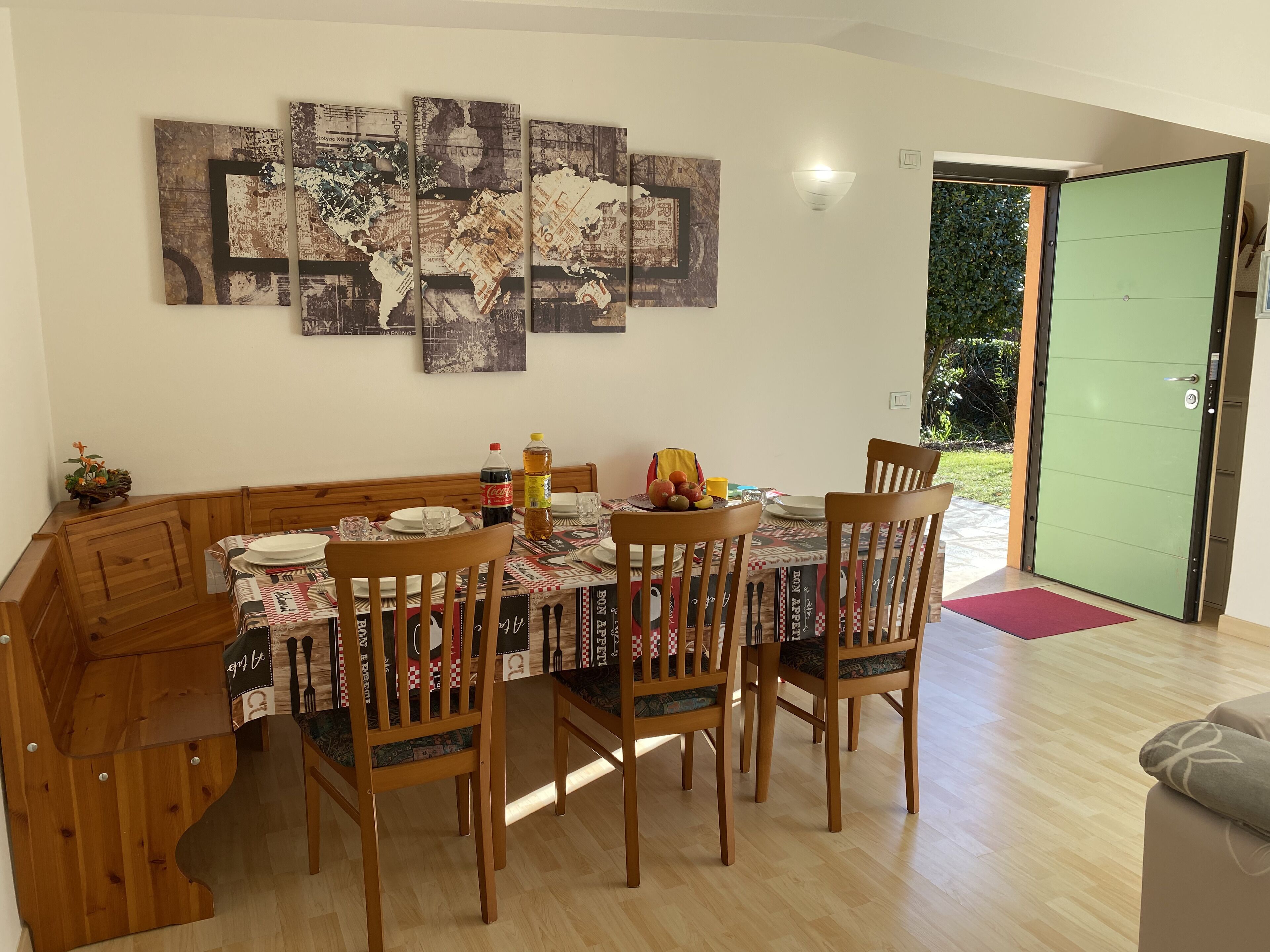 Un comedor con una mesa de madera dispuesta para cuatro personas, rodeada de sillas. Una gran obra de arte abstracta se exhibe en la pared sobre la mesa.