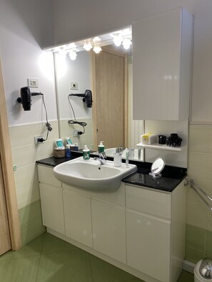 Un baño con lavamanos, espejo, secador de pelo y distintos artículos de aseo.