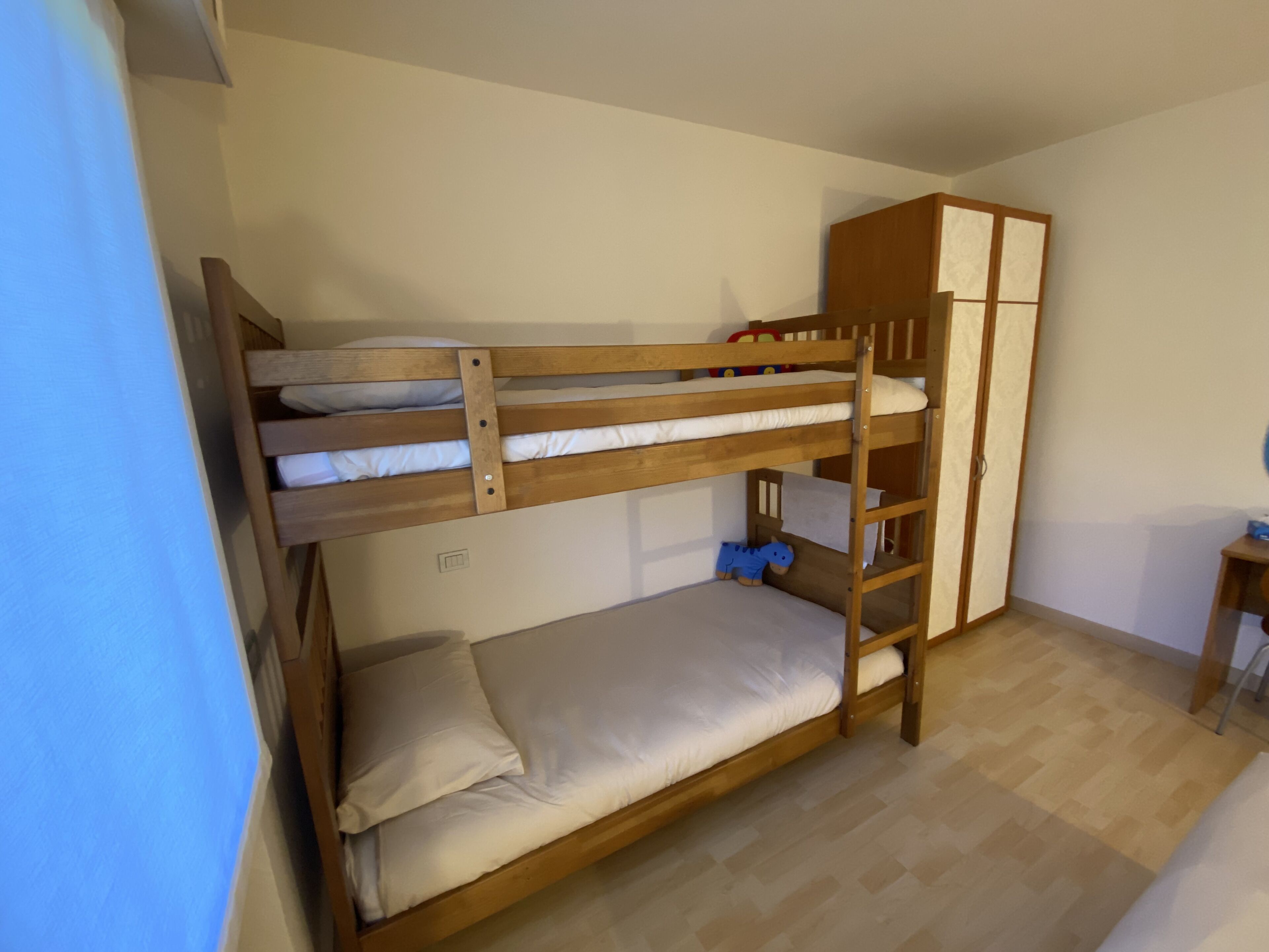 Habitación con literas, un armario de madera y una mesita pequeña.