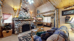 Interior acogedor de una cabaña de troncos con chimenea de piedra, muebles de madera y un televisor.