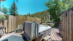 Un jacuzzi en una terraza de madera con un cerco de madera y árboles al fondo.