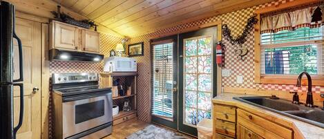 A compact kitchen with wooden cabinets, a stove, a microwave, and a sink.