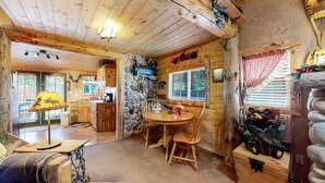 Interior rústico de una cabaña con pared de piedra, una mesa de comedor de madera y una acogedora chimenea.