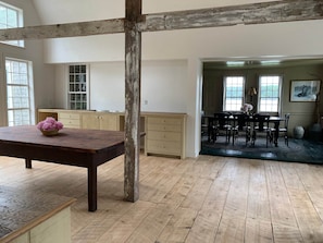 A spacious room with a wooden floor, a dining area with a table and chairs, and a kitchen area with cabinets and a window. - Coasters' Chance - The Maine Cottage (Cutler)