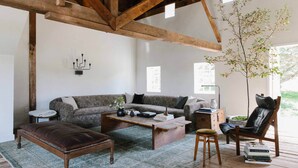 Un salon chaleureux avec un plafond en bois, un canapé, une table basse, un pouf en cuir, un fauteuil et une bibliothèque.