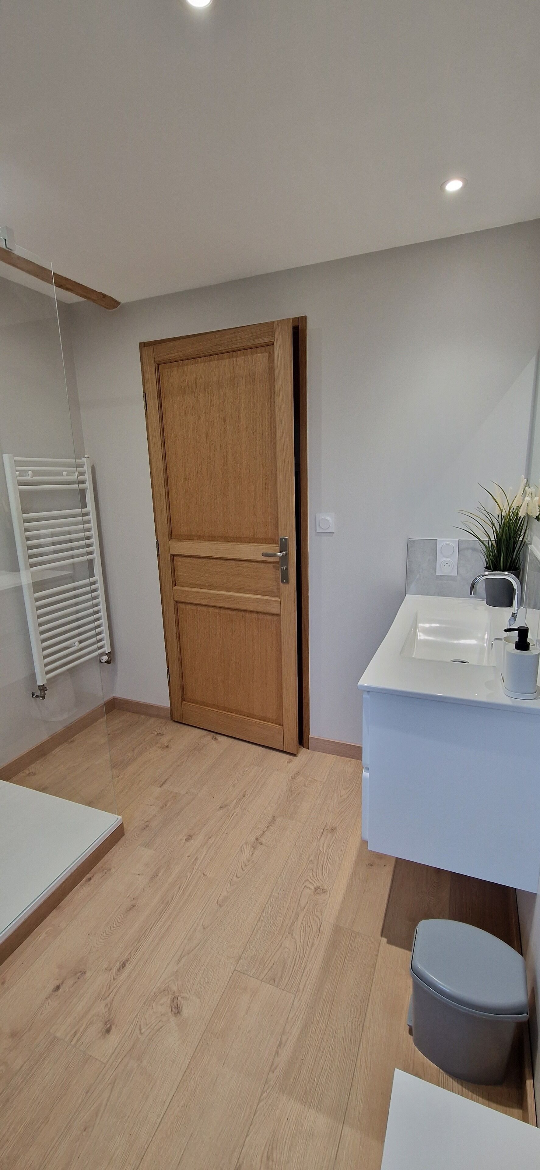 Un bagno moderno con porta in legno, lavandino bianco e un piccolo cestino.