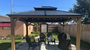 A covered patio area with two Adirondack chairs, a barbecue grill, and a pergola structure. - 7 mins to the beach (Delray Beach)