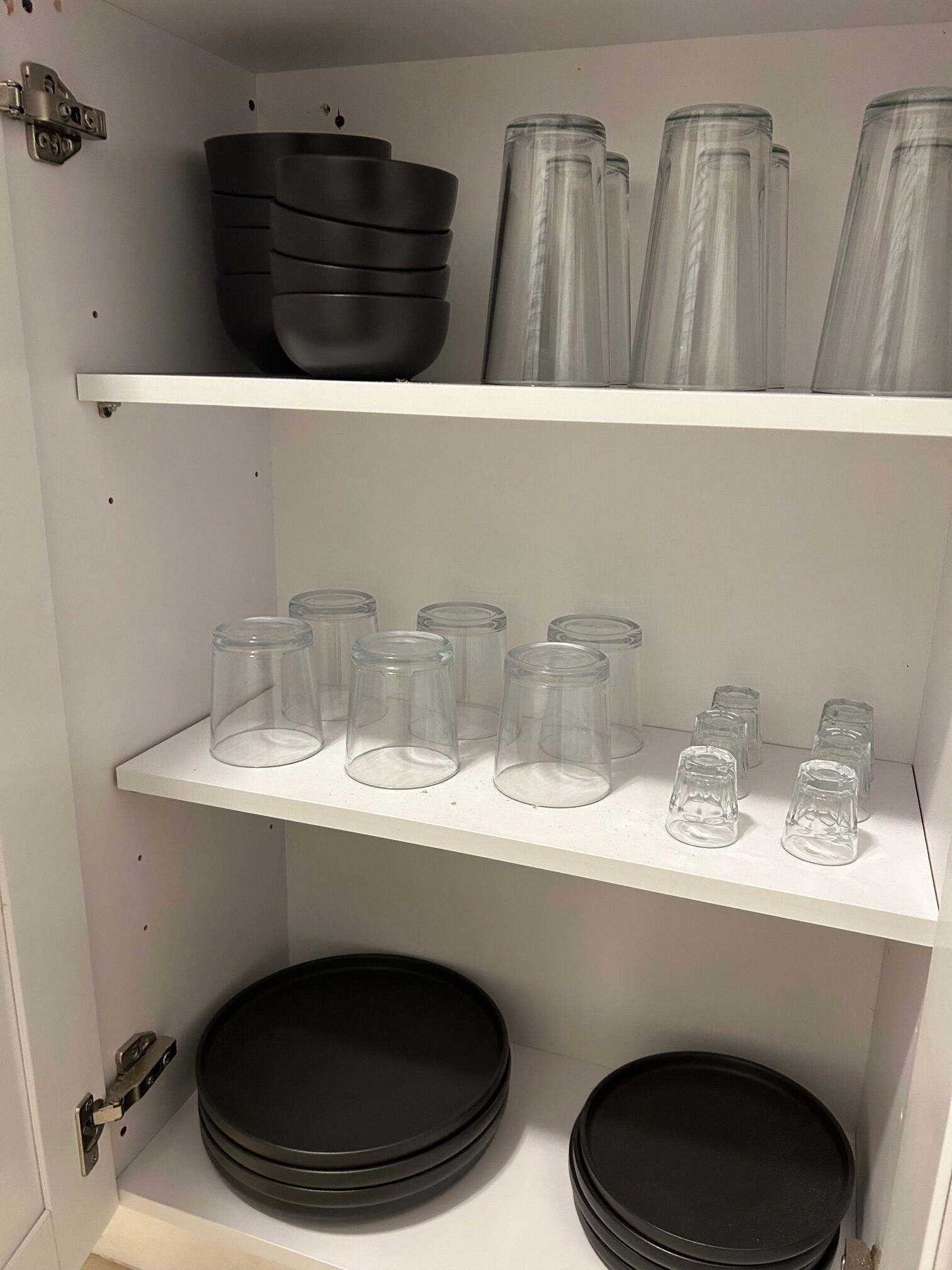 A kitchen with white shelves holding black bowls, clear glass pitchers, and clear glass cups.