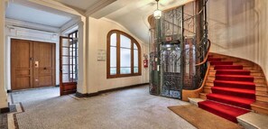 A grand staircase with red carpet, a wooden door, and a glass elevator.
