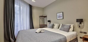 A hotel room with a large bed, a bedside table, a wall-mounted lamp, and a window with curtains.