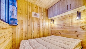 A wooden-paneled room with a bed, a wall-mounted light fixture, and a framed picture. - Apollo - au coeur du Corbier (Villarembert)