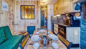 A cozy kitchen with wooden walls, a dining table set for four, and a green sofa. - Apollo - au coeur du Corbier (Villarembert)