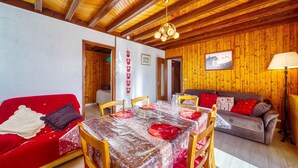 A cozy room with a wooden ceiling, a dining table set with red plates and glasses, a red sofa, and a grey couch. - Chalet les Colchiques (Fontcouverte-la-Toussuire)