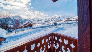 A snowy mountain landscape with a wooden balcony overlooking a snow-covered road and buildings. - Chalet les Colchiques (Fontcouverte-la-Toussuire)