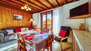 A cozy room with wooden walls and ceiling, a dining table set with red plates, and a TV mounted on the wall. - Chalet les Colchiques (Fontcouverte-la-Toussuire)