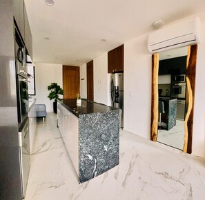 A modern kitchen with a marble countertop, stainless steel appliances, and wooden cabinets. - Cruz 504: Studio w Rooftop Pool, 2 Blocks to Beach (Cruz de Huanacaxtle)