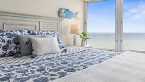 Une chambre avec un grand lit, une vue sur l’océan, un décor sur le thème des poissons et une lampe sur une table de chevet.