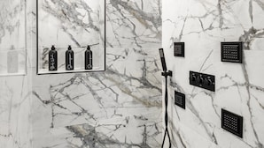 Une salle de bain moderne avec des murs en marbre, un grand miroir et plusieurs pommes de douche.