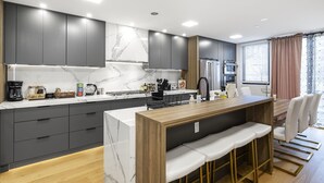 Une cuisine moderne avec des meubles de couleur sombre, un pare-feu en marbre et un îlot central en bois doté de tabourets de bar.