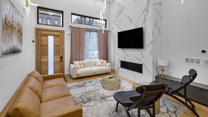 Un salon moderne avec un canapé, des fauteuils, une table basse et un téléviseur fixé au mur.