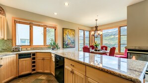 A spacious kitchen with wooden cabinets, granite countertops, and a dining area with red chairs. - Slopeside Chalet 3 Bedroom Townhouse by Alpine Lodging Telluride (Telluride)