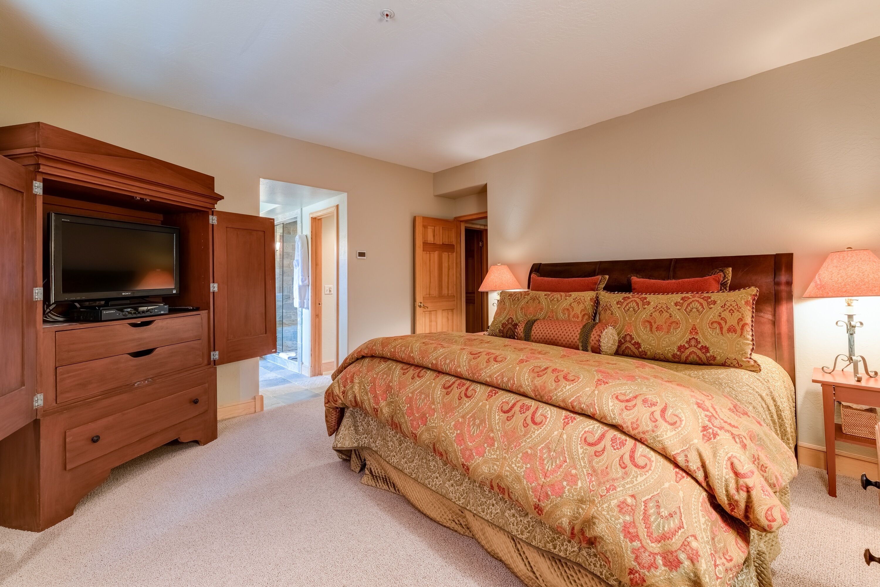 A bedroom with a large bed, wooden dresser, TV, and a lamp.