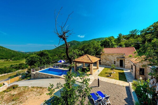 A villa with a swimming pool, a stone building, and a view of the surrounding hills.