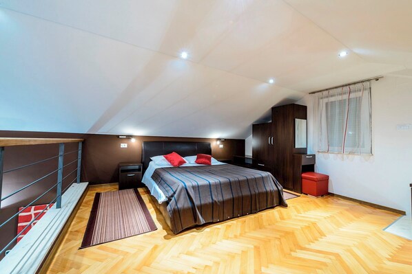 A bedroom with a bed, nightstands, a wooden floor, and a window with curtains.