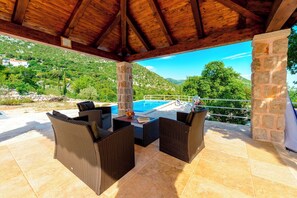 An outdoor patio with wicker furniture, a stone pillar, and a view of a pool and mountains.
