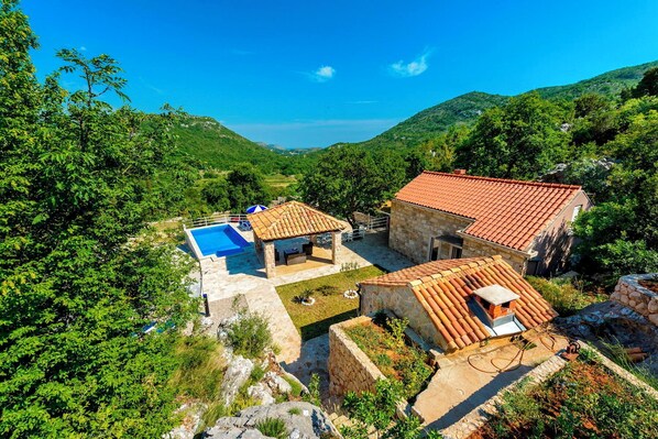A villa with a swimming pool, stone walls, and terracotta roofs.