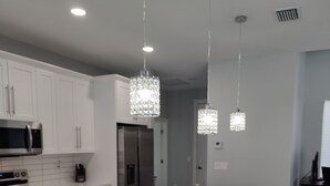 A modern kitchen with white cabinets, stainless steel appliances, and pendant lighting.