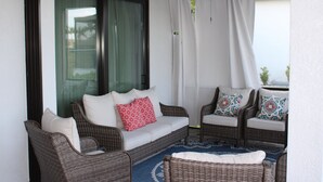 A balcony with wicker furniture, including a sofa and two chairs, and a blue patterned rug.