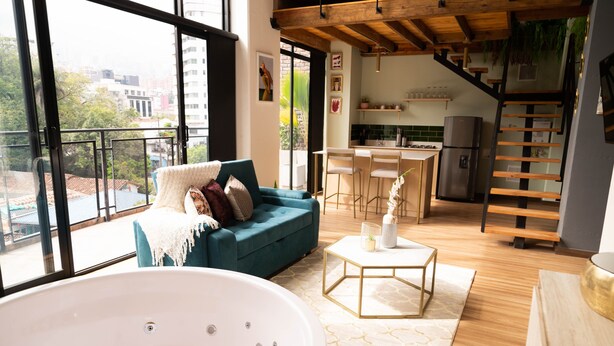 Un espacio habitable moderno con un amplio ventanal, un sofá azul, una bañera blanca y una zona de cocina.