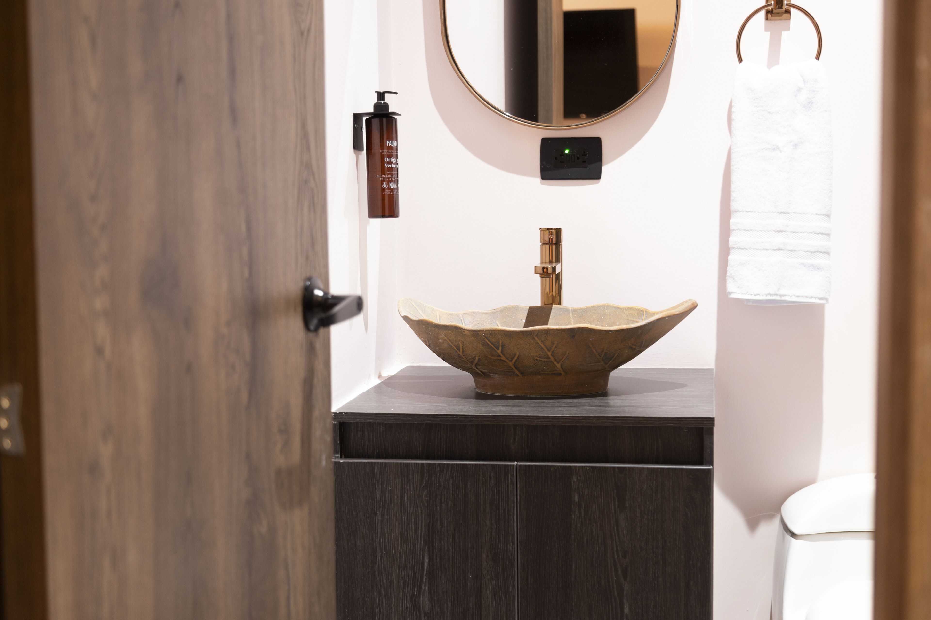 A bathroom with a wooden door, a round mirror, a sink with a unique bowl design, and a towel hanging on a ring.