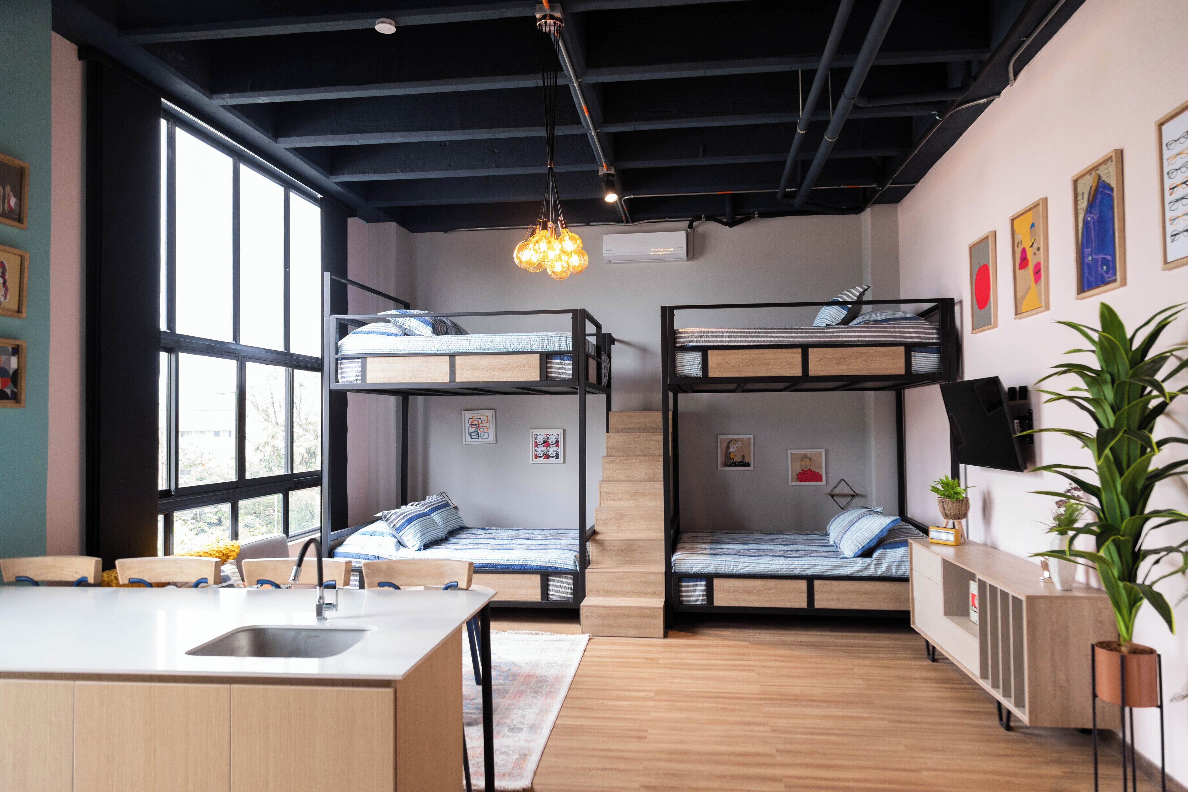 A modern, well-lit room with bunk beds, a kitchen area, and large windows.