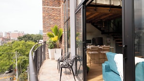 Un balcón con vista a la ciudad, un comedor con sillas y una mesa, y un sofá azul.