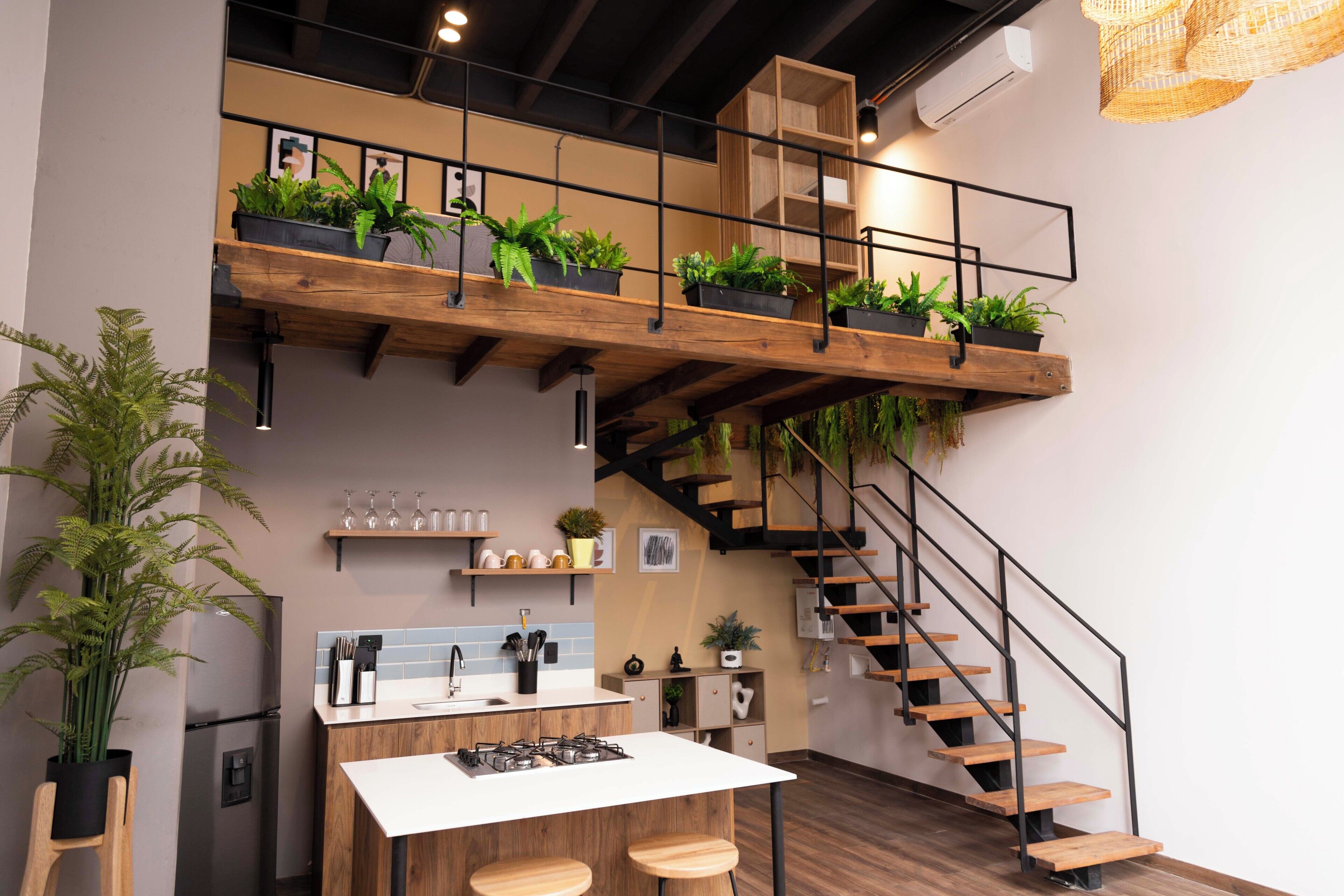 A modern kitchen with a central island, wooden staircase, and potted plants.