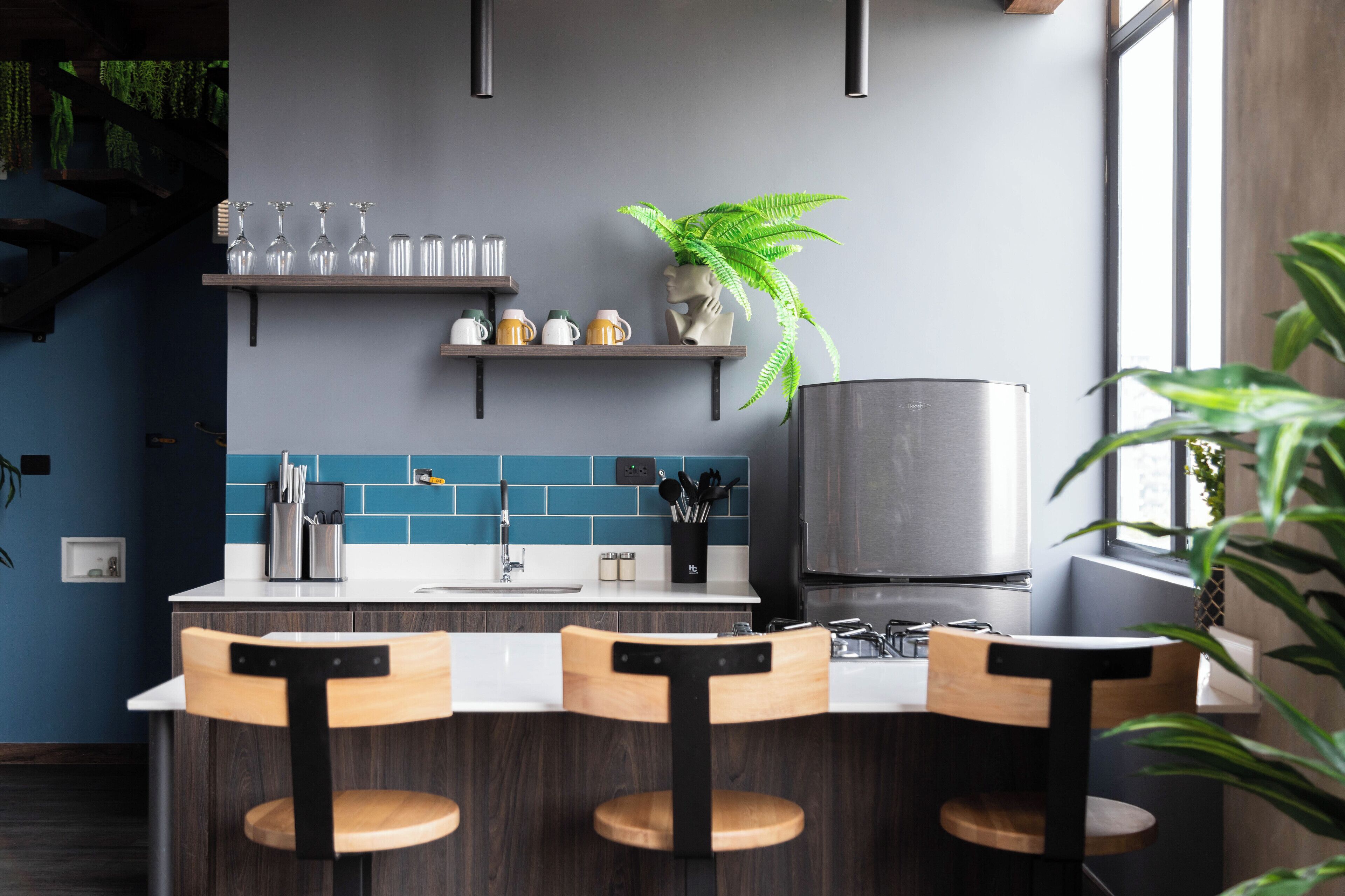 Una cocina moderna con barra, que incluye un refrigerador de acero inoxidable, salpicadero de azulejos azules y taburetes de bar de madera.