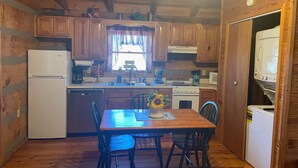 Una cucina compatta con mobili in legno, un frigorifero, un lavandino, un fornello e un forno a microonde. C'è un tavolo da pranzo con sedie e un vaso di fiori.