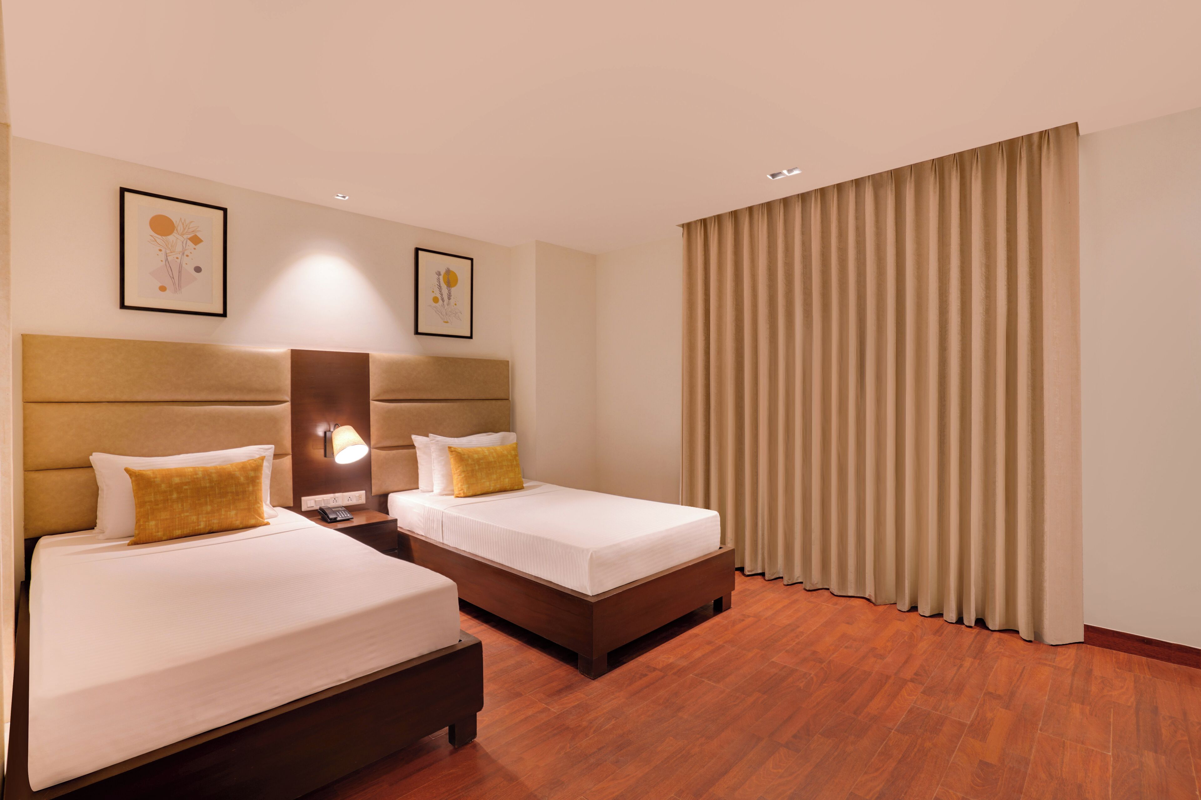 A hotel room with two beds, a nightstand with a lamp, and a large window with curtains.