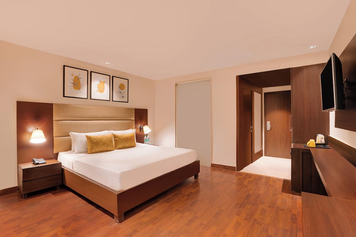 A hotel room with a large bed, wooden flooring, a desk with a flat-screen TV, and framed artwork on the wall.