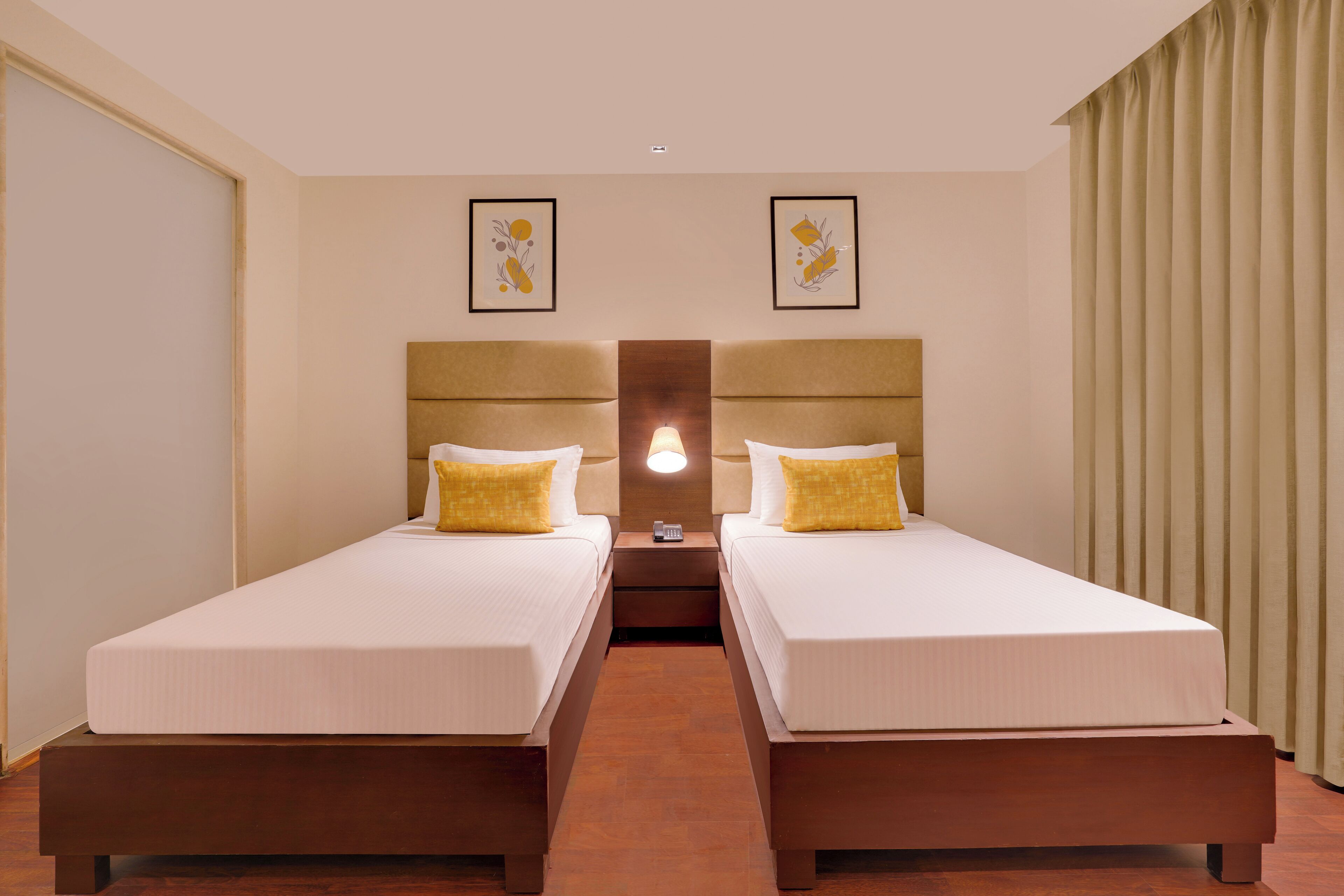 A hotel room with two single beds, a nightstand with a lamp, and a large window with curtains.