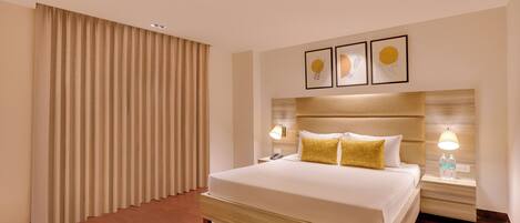 A modern hotel room with a large bed, two bedside tables with lamps, a headboard with artwork, and a large window with curtains.